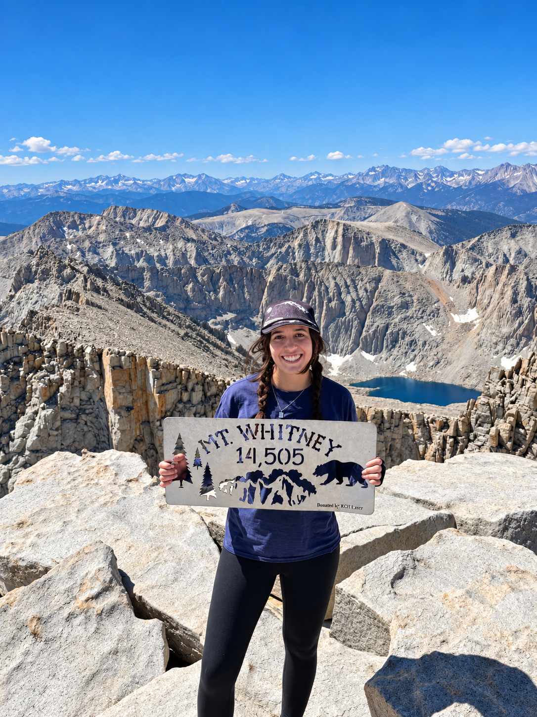 Priya Merrill holding a Mount Whitney summit sign with mountains behind her